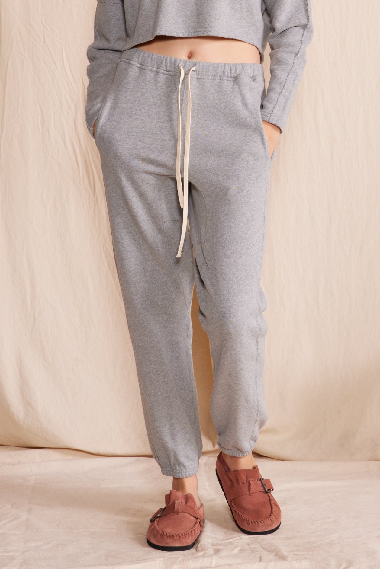 Person wearing gray jogger pants and brown shoes on a beige background