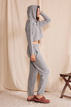 Person wearing a gray hoodie and pants standing against a beige curtain.
