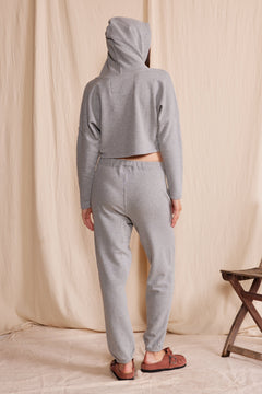 Person wearing a gray hoodie and pants standing against a beige curtain.