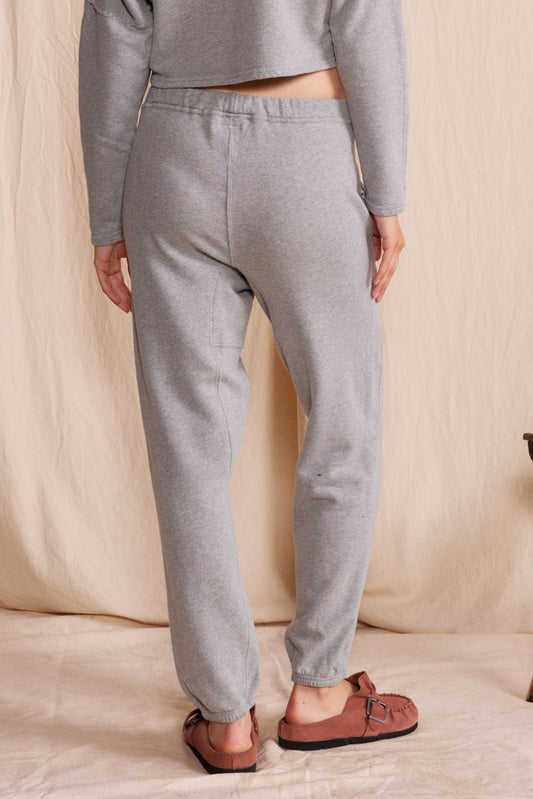 Person wearing gray sweatpants and a cropped top on a beige background