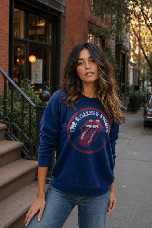 A woman wearing a navy blue crewneck sweatshirt with a large red and white 'The Rolling Stones' graphic on the front, standing on a city sidewalk.