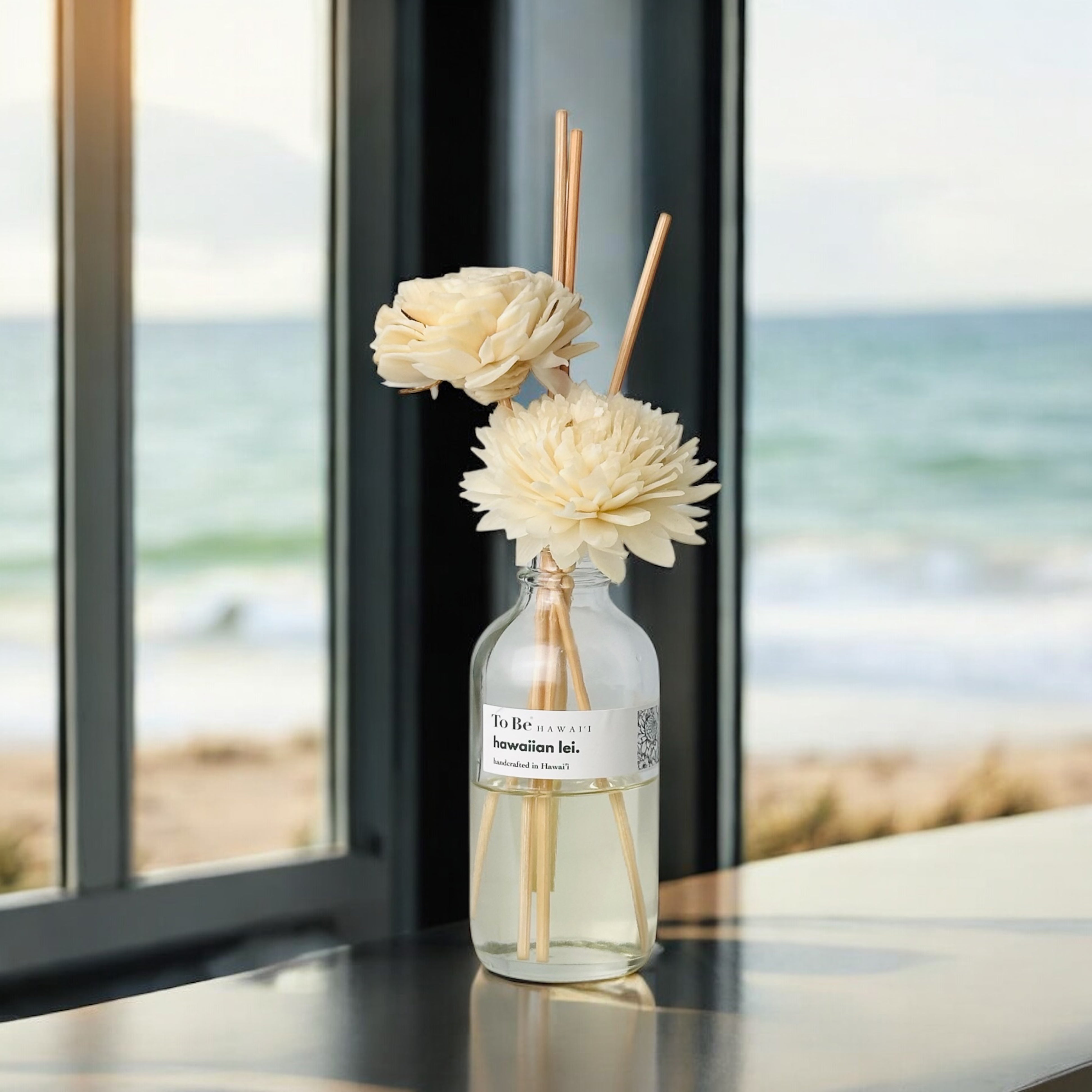 Decorative diffuser with flowers on a table by a window with a beach view