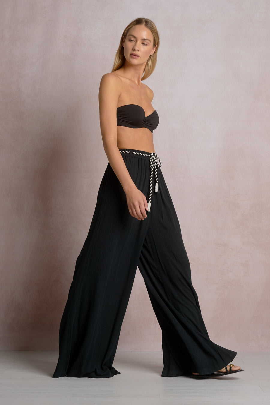 Woman wearing a black strapless top and wide-leg pants against a neutral background