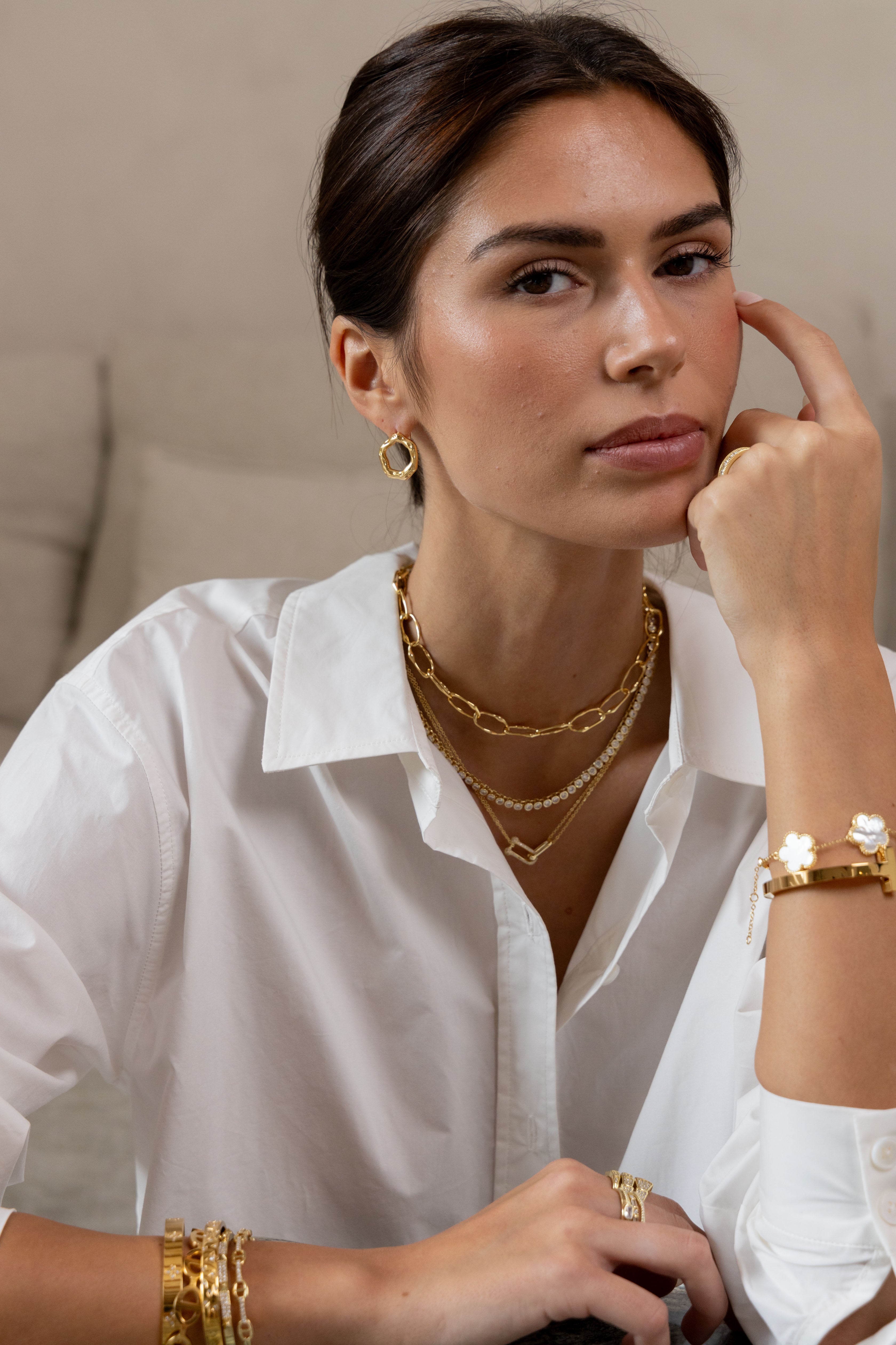 Woman wearing gold jewelry including necklaces, bracelets, and earrings.