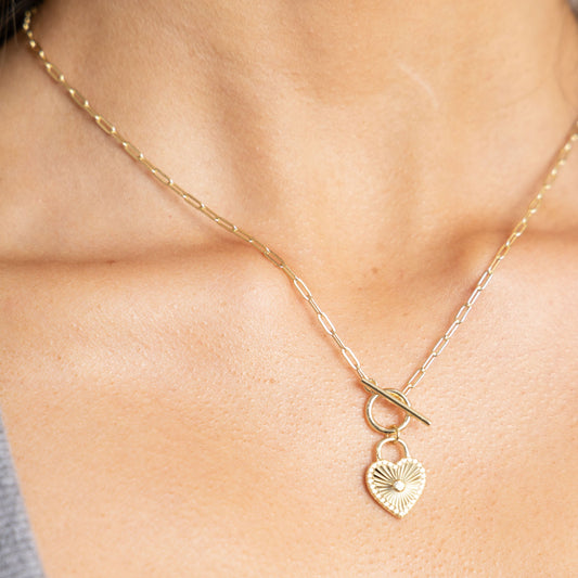 Gold necklace with a heart-shaped pendant on a person's neck