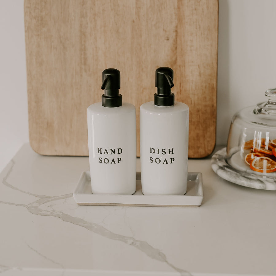 Two white soap dispensers labeled 'Hand Soap' and 'Dish Soap' on a marble surface with a wooden cutting board in the background.