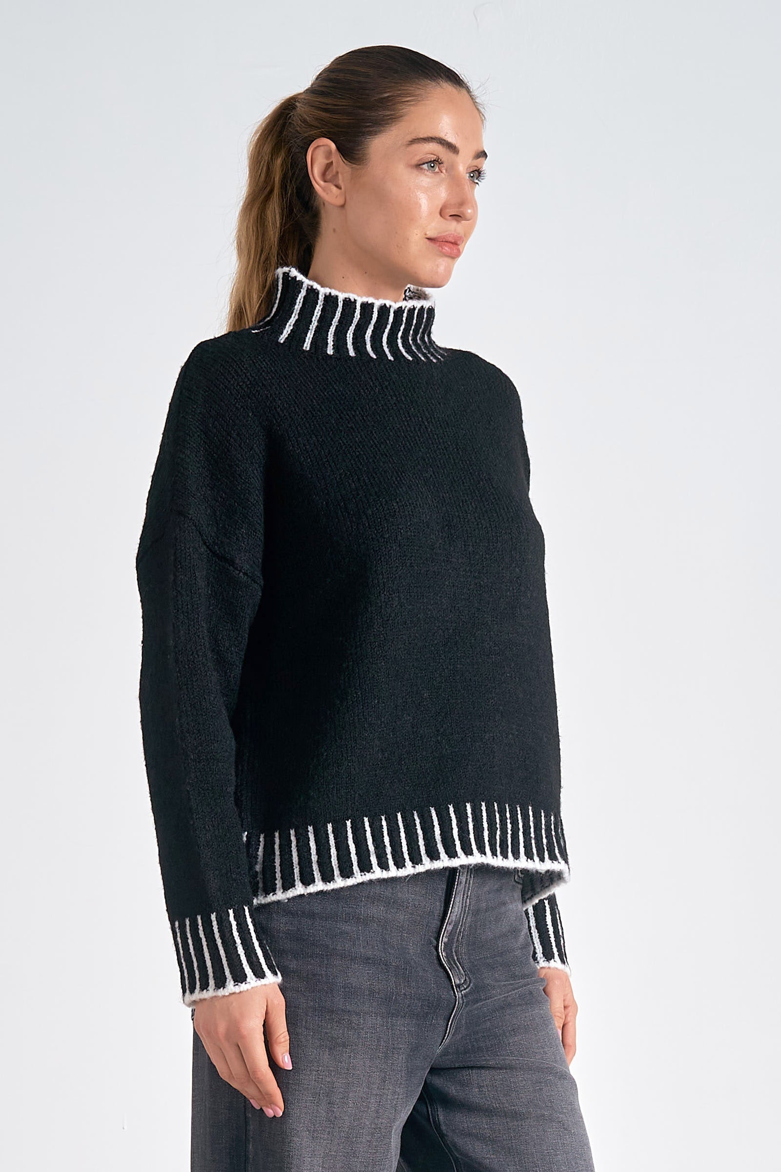 Woman wearing a black sweater with white trim on a plain background