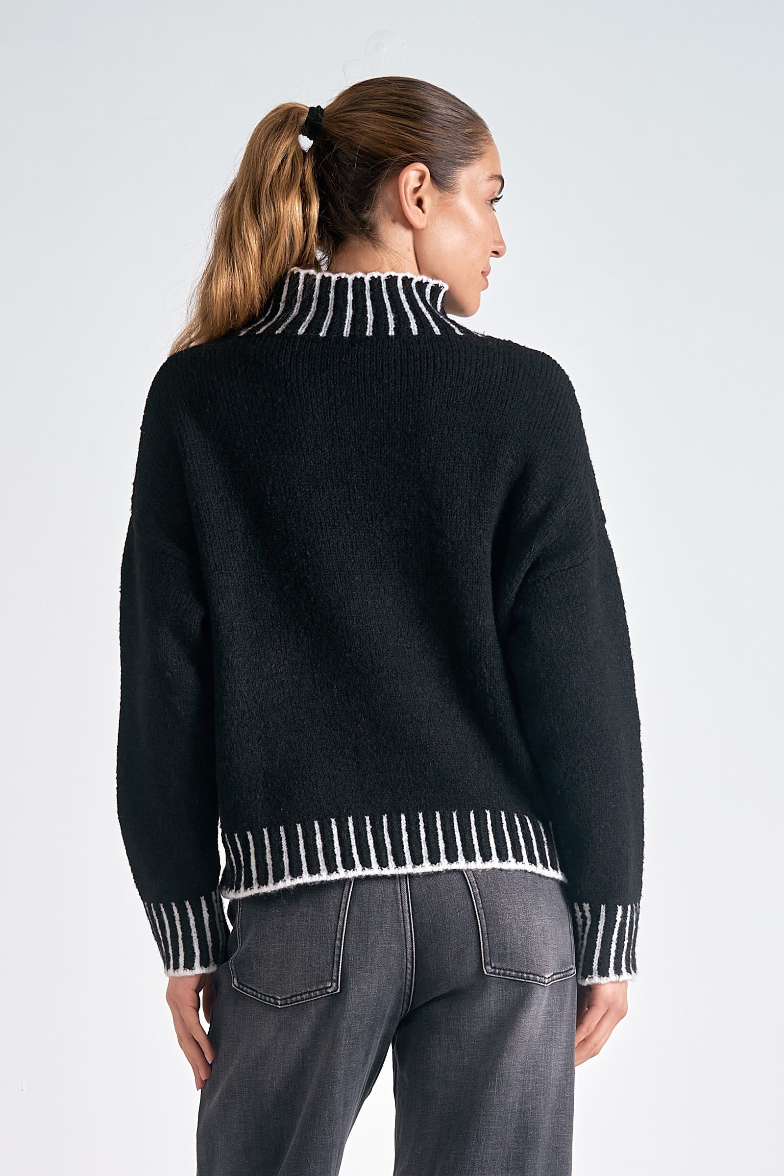 Person wearing a black sweater with white trim on a plain background
