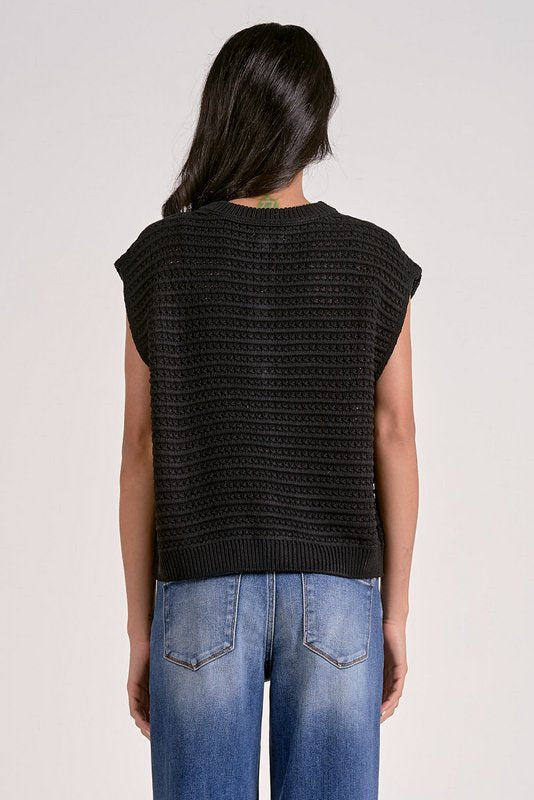 Person wearing a black sleeveless knitted top and blue jeans on a white background