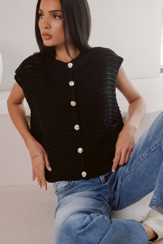 Woman wearing a black knitted vest with silver buttons and blue jeans.