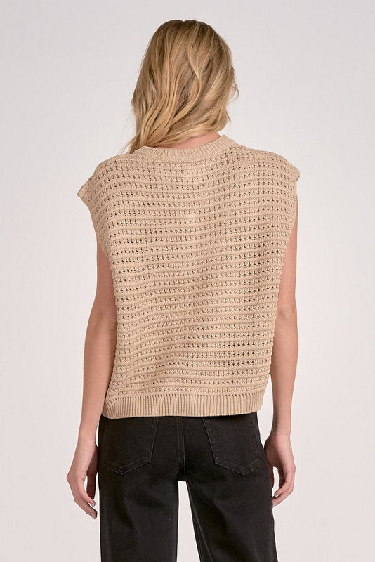 Person wearing a beige knitted vest on a plain background