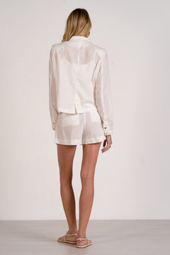 Woman wearing a white outfit with a jacket and shorts on a plain background