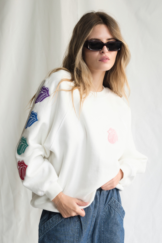 Woman wearing a white sweater with colorful designs and sunglasses against a plain background
