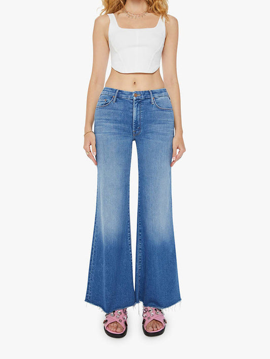 Woman wearing Mother jeans Work Hard Play Hard the Roller Fray blue flared jeans and a white crop top on a white background