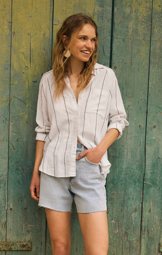 Woman wearing a striped shirt and shorts standing against a textured green wall.