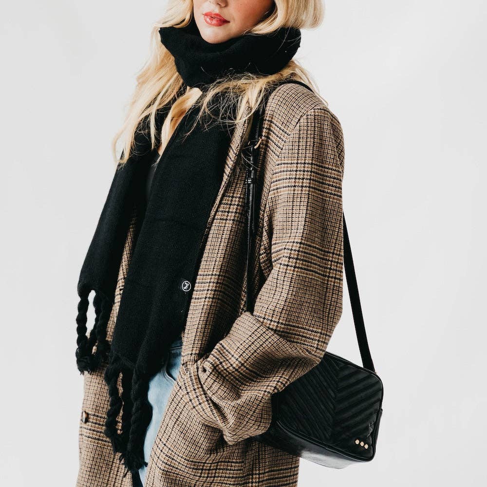 Person wearing a plaid coat with a black scarf and carrying a black handbag on a light gray background