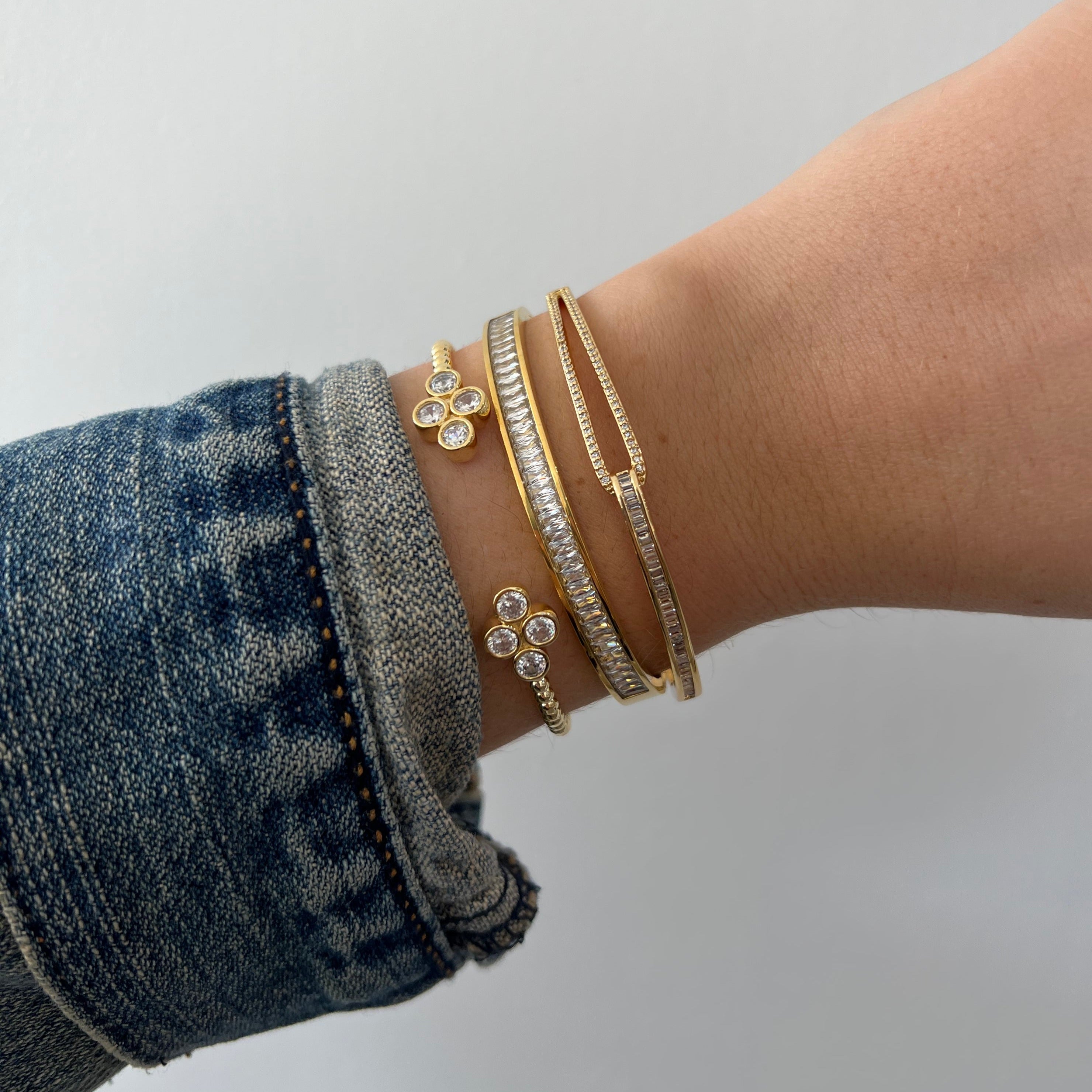 Close-up of a wrist wearing gold bracelets on a plain background