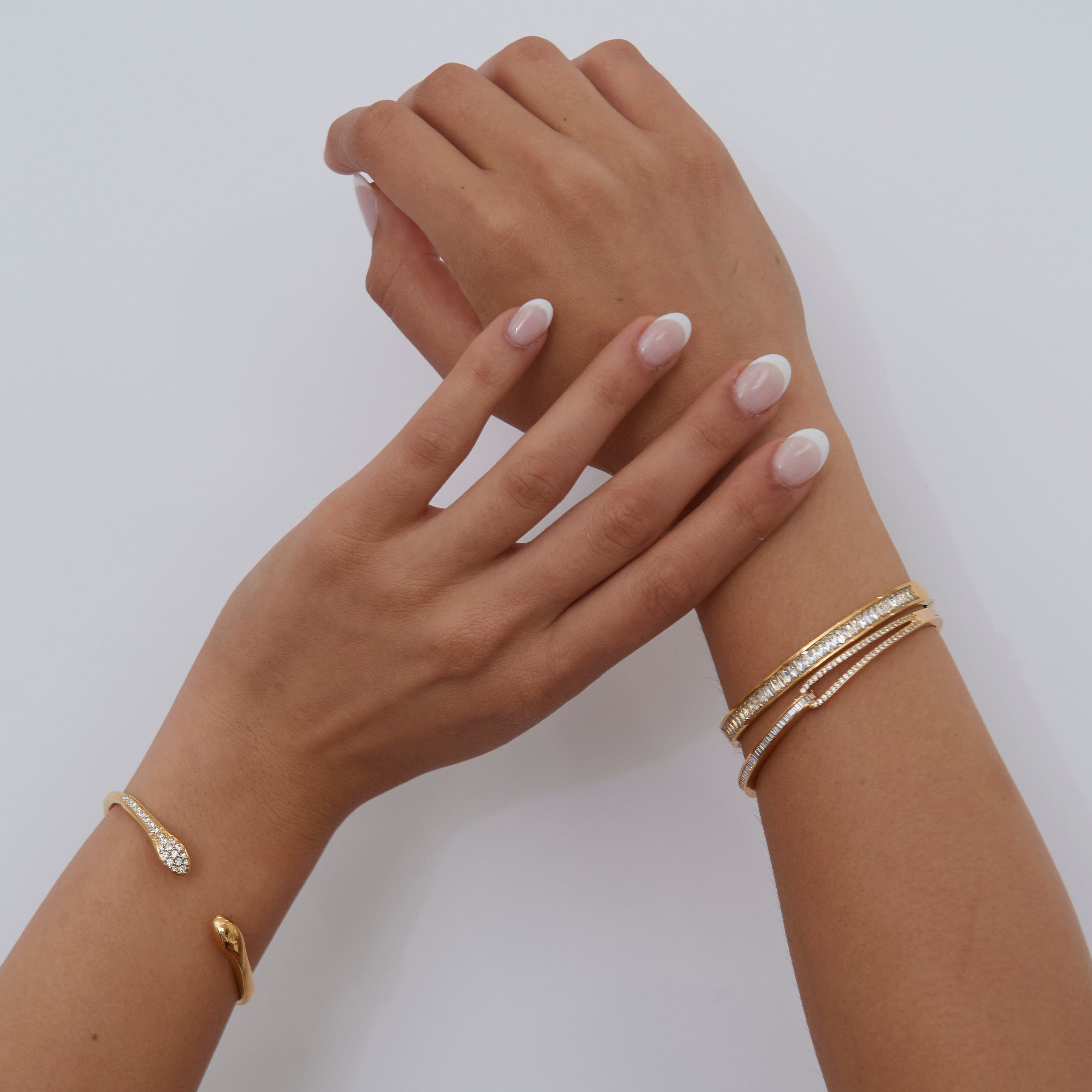 Two hands with gold bracelets on a plain background