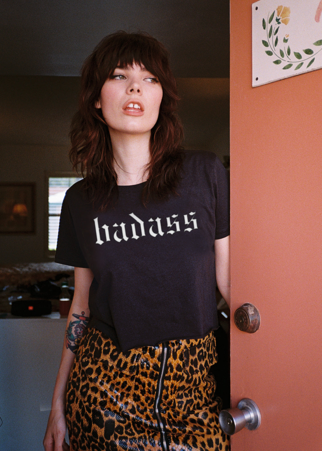 Person wearing a black t-shirt with 'badass' text, standing in a room.