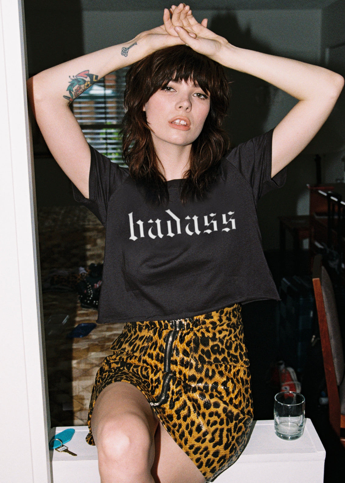 Person wearing a black t-shirt with 'haddass' text and a leopard print skirt indoors.