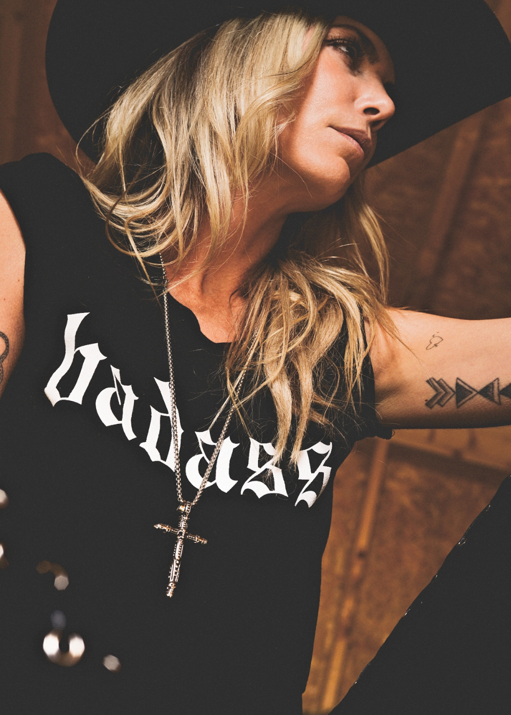 Person wearing a black tank top with 'badass' text and a cross necklace.