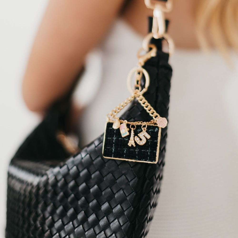 Black woven handbag with a gold charm featuring letters on a blurred background