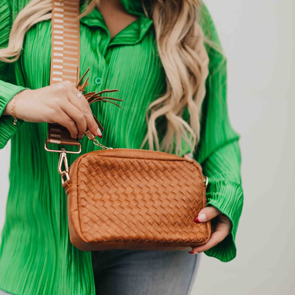 Person holding a brown woven handbag with a green top.