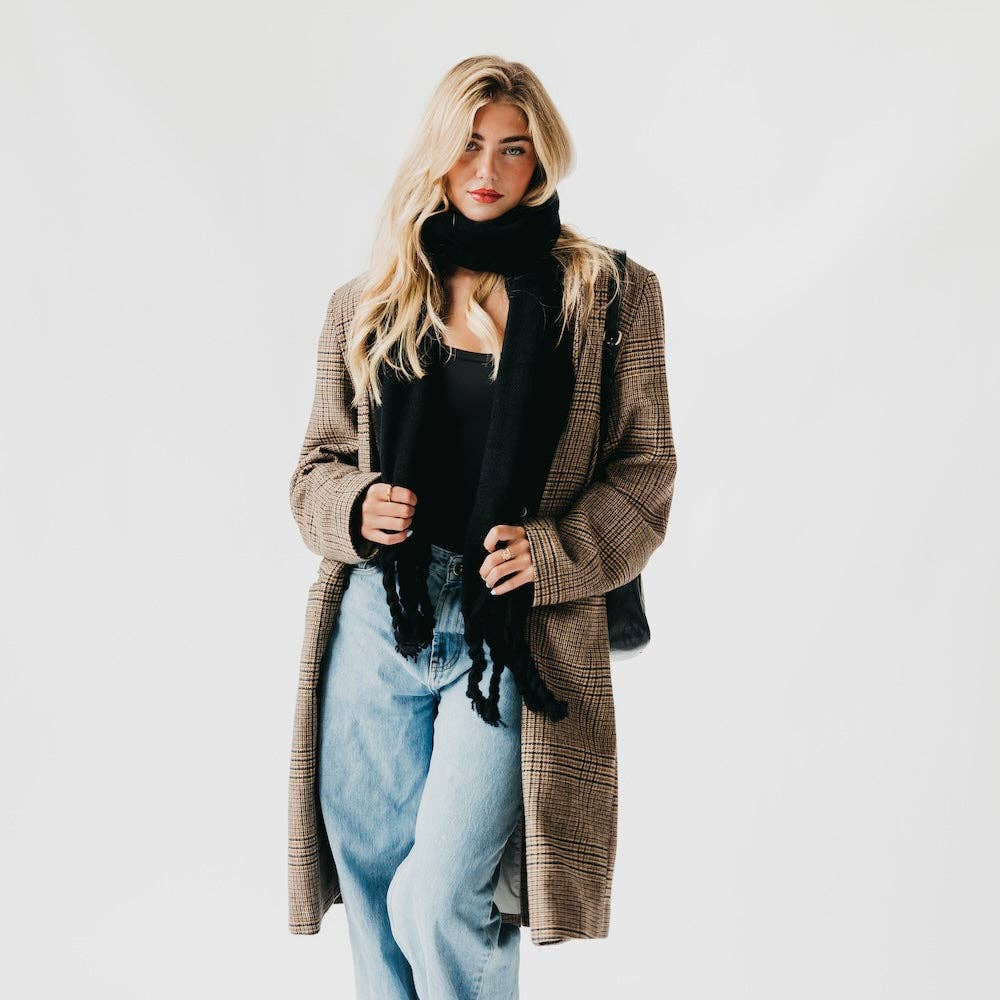 Woman wearing a plaid coat, black scarf, and light blue jeans on a white background
