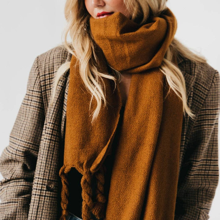 Person wearing a caramel colored scarf and plaid coat on a white background