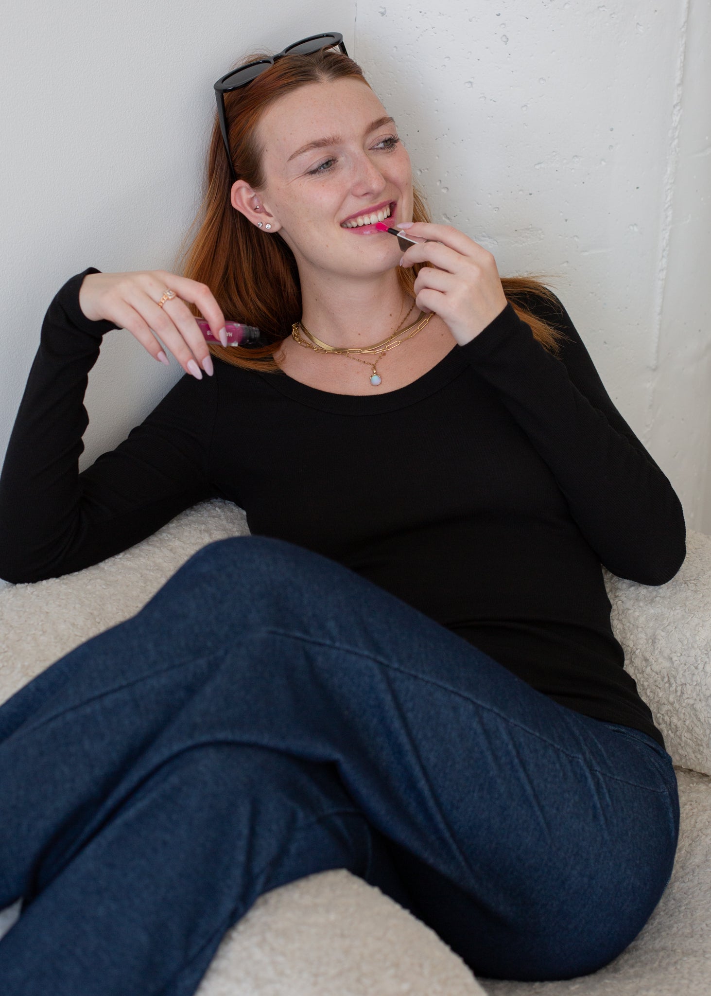 Woman sitting on a couch applying lipstick with a neutral background