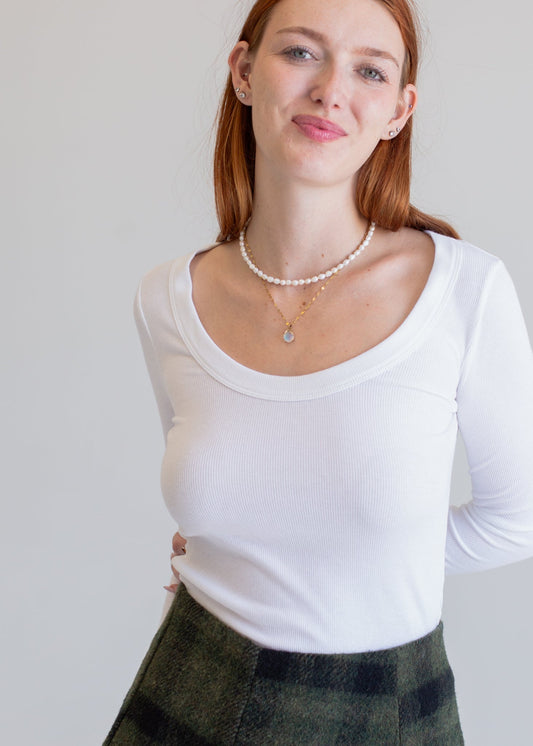 Woman wearing a white long-sleeve top and plaid skirt against a plain background