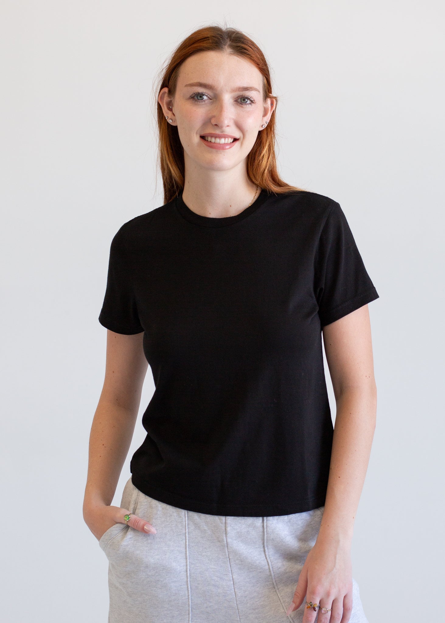 Woman wearing a black t-shirt and light gray pants against a white background