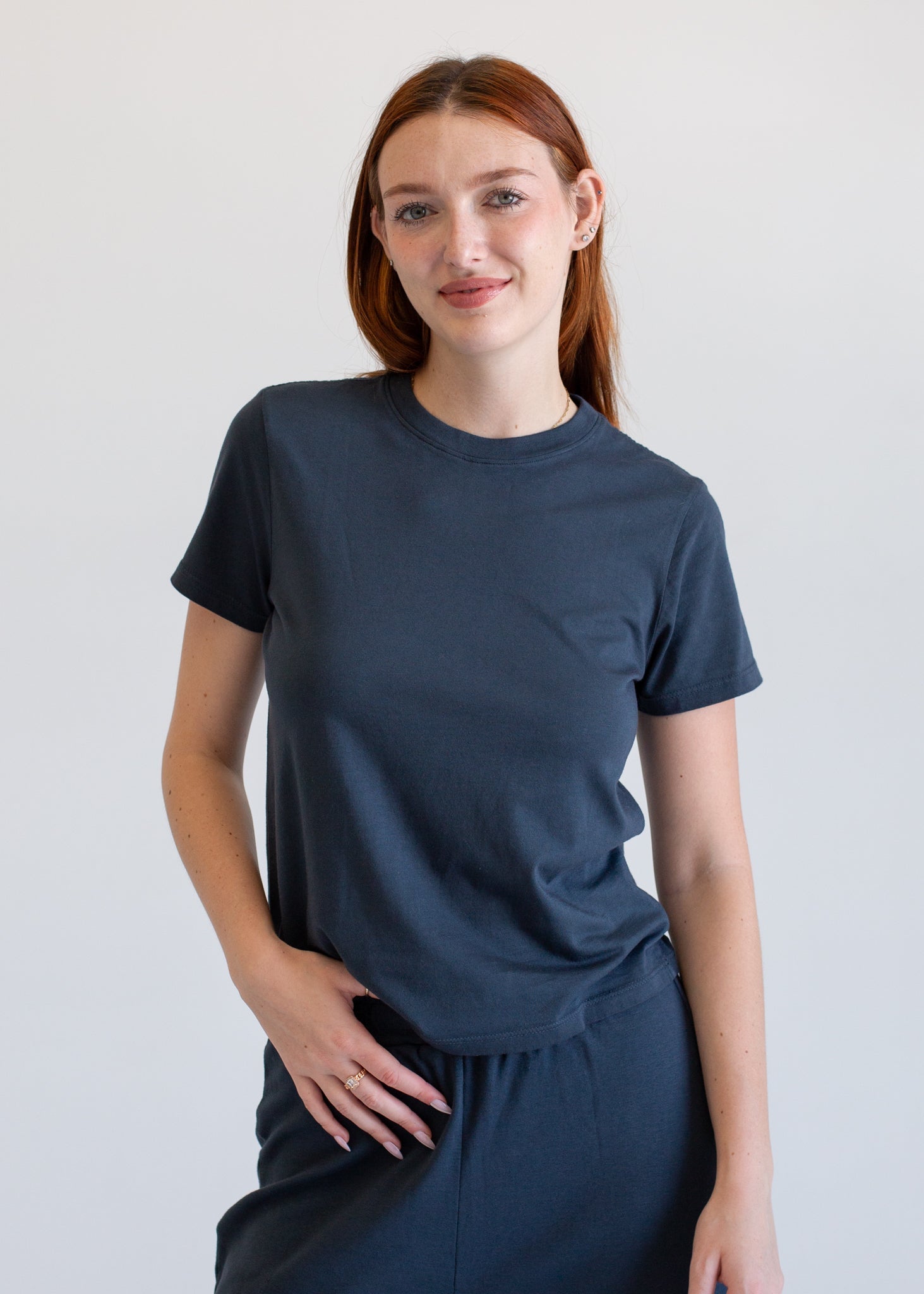 Woman wearing a black t-shirt and light gray pants against a white background