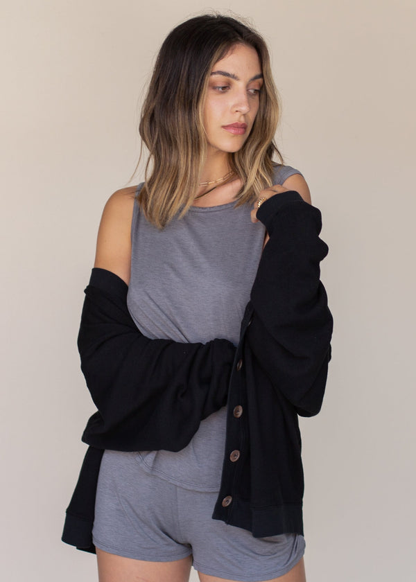 Woman wearing a black cardigan over a gray top and shorts on a beige background