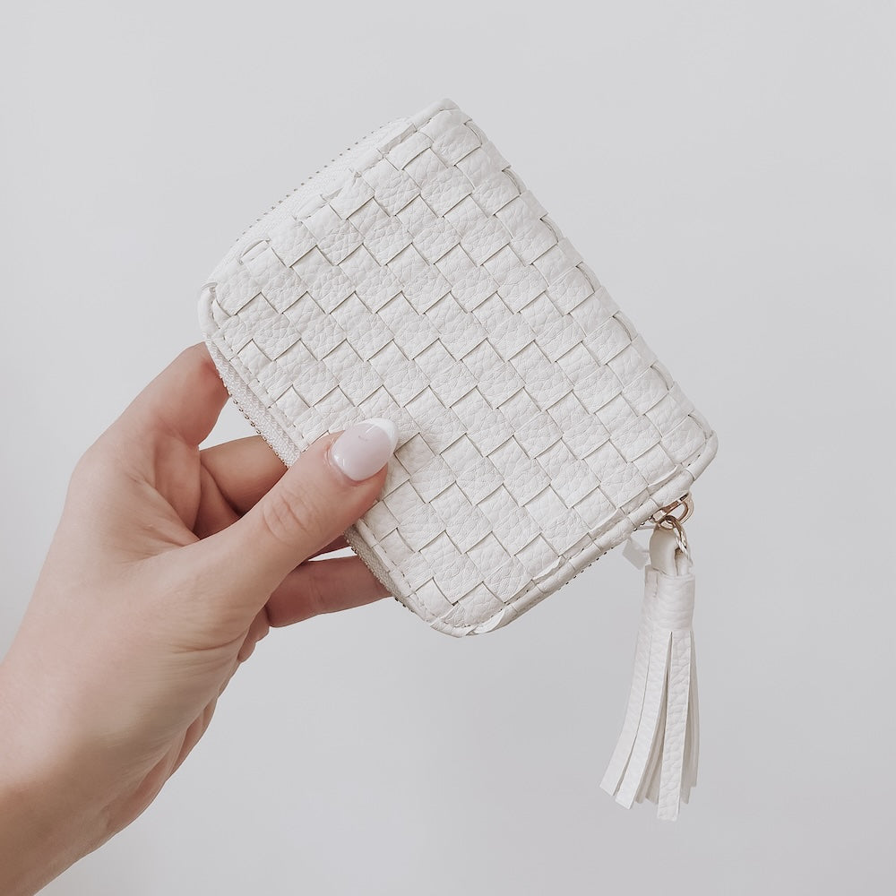 Hand holding a woven white clutch bag against a plain background