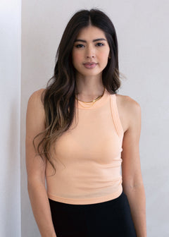 Woman wearing a peach tank top against a plain background