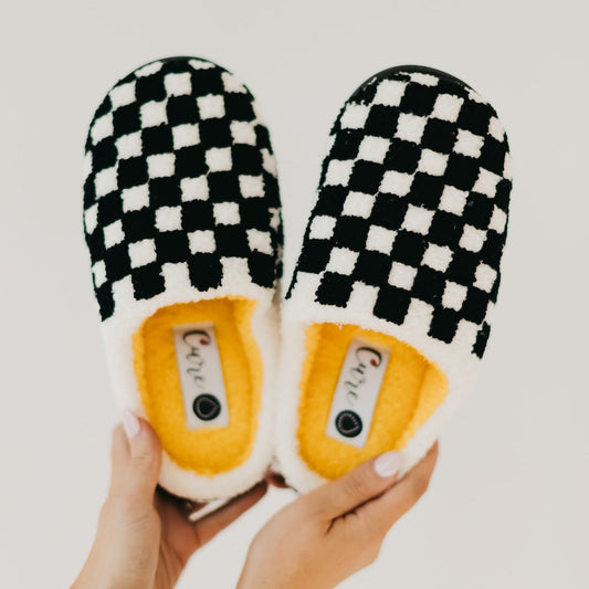 Black and white checkered slippers with yellow soles held by a person on a light gray background
