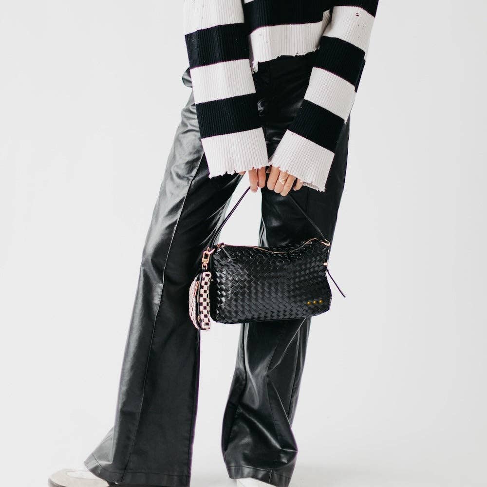 Person wearing a black and white striped sweater and holding a black handbag on a white background