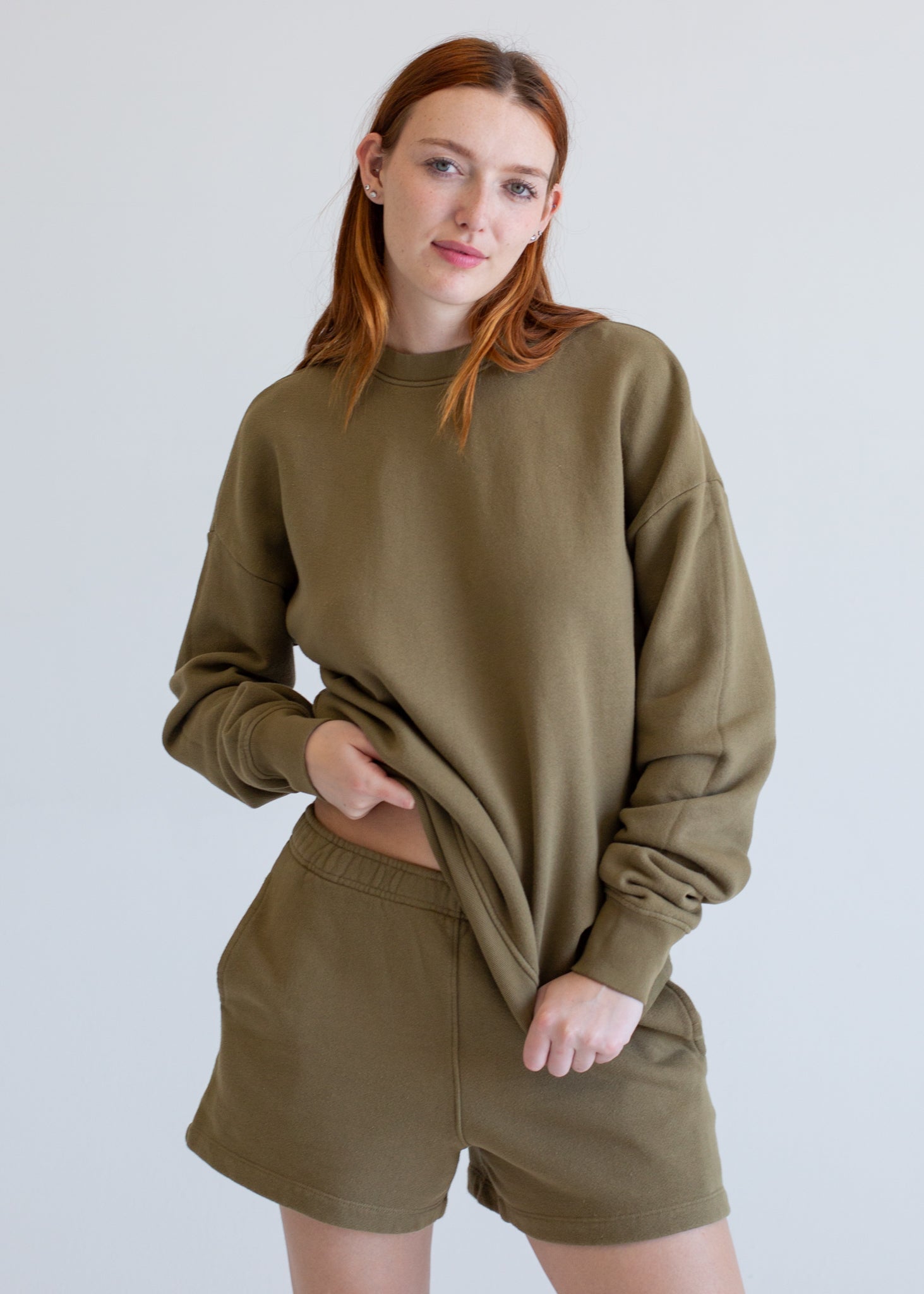 Woman wearing an olive green sweatshirt and shorts set against a plain background