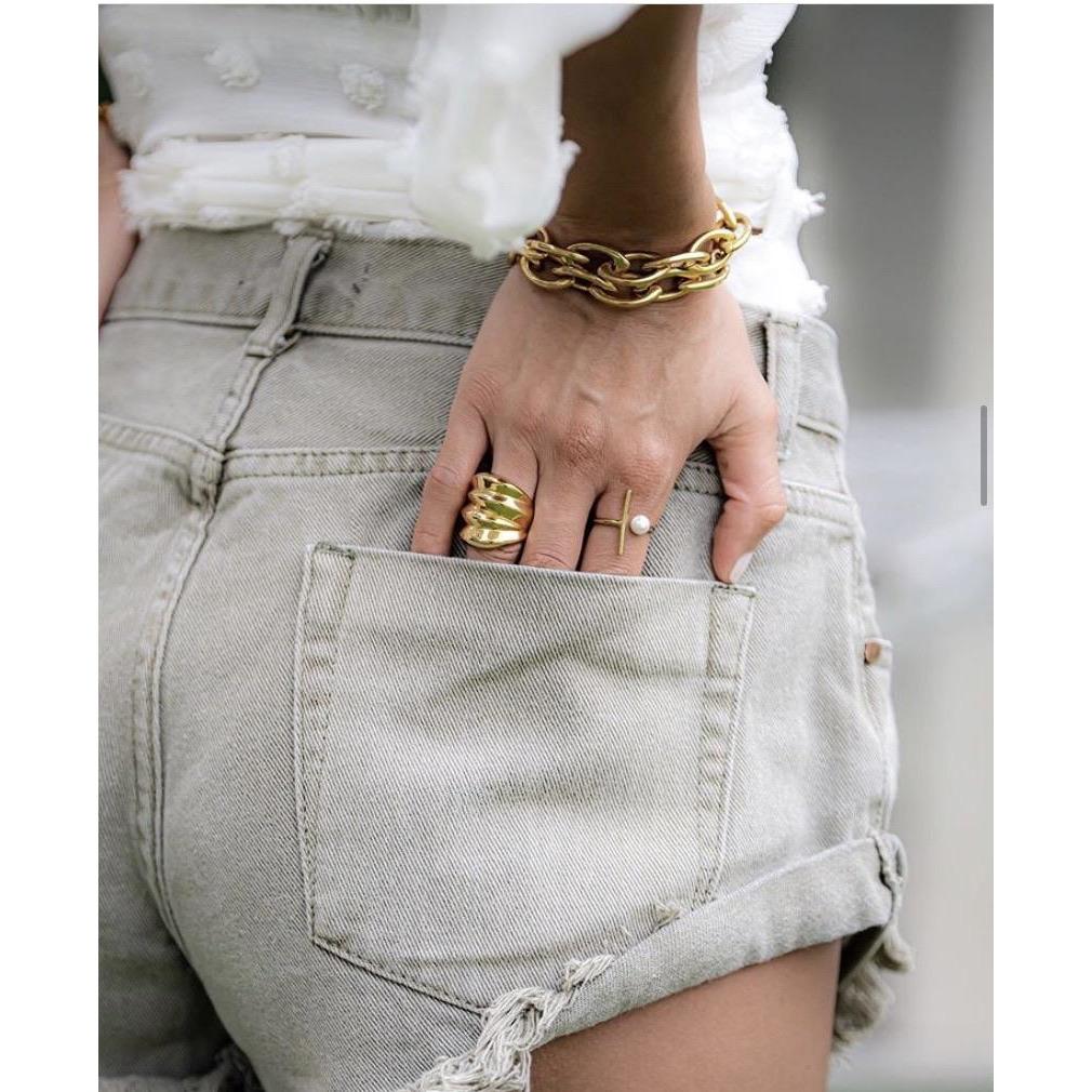 Person wearing gold bracelets and rings with light gray denim shorts.