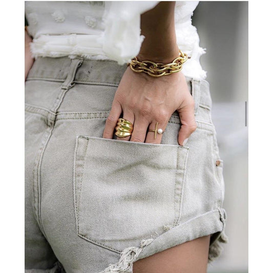Person wearing gold bracelets and rings with light gray denim shorts.