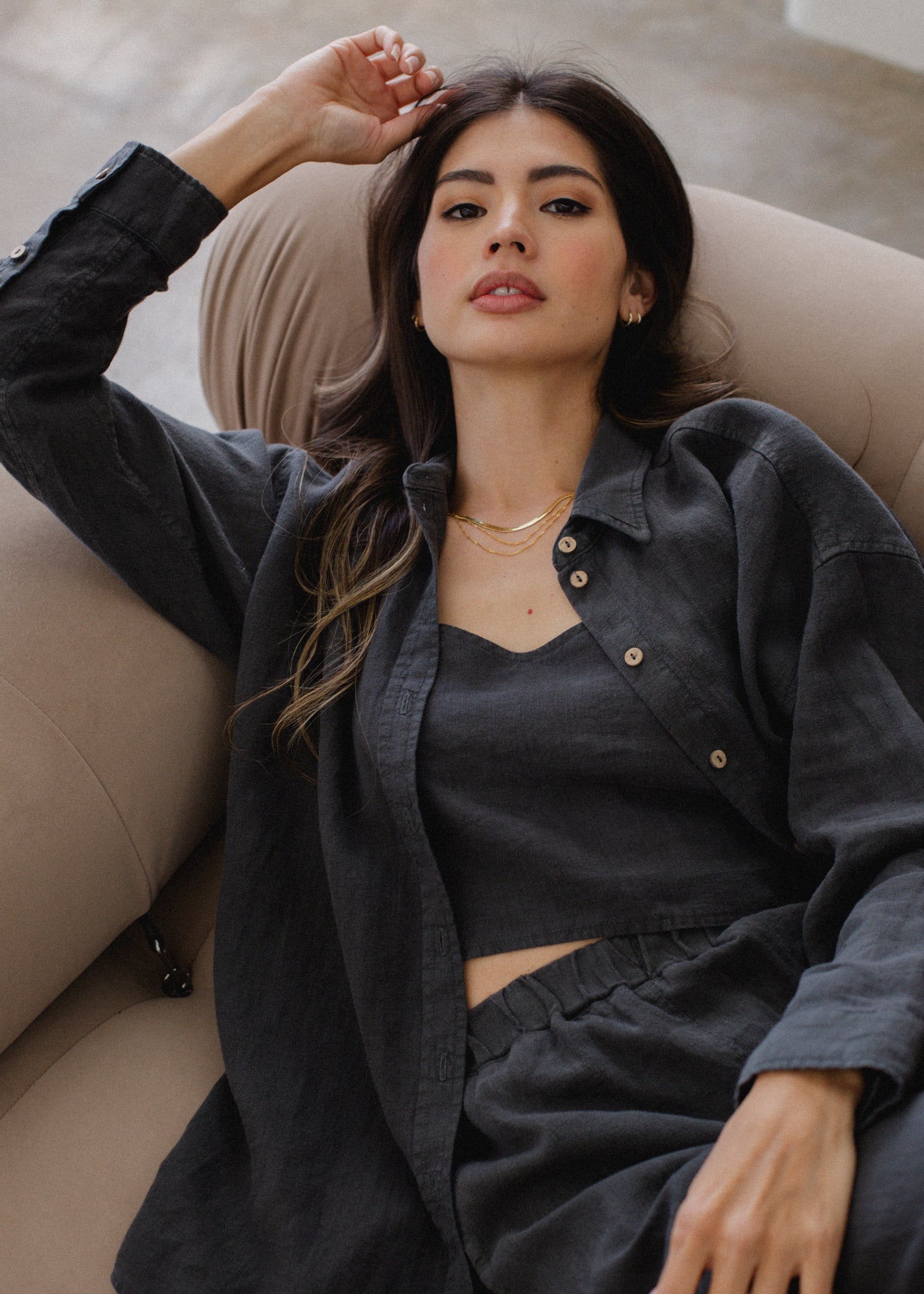 Woman laying on couch wearing black long sleeved linen shirt, linen tank and linen pull on shorts