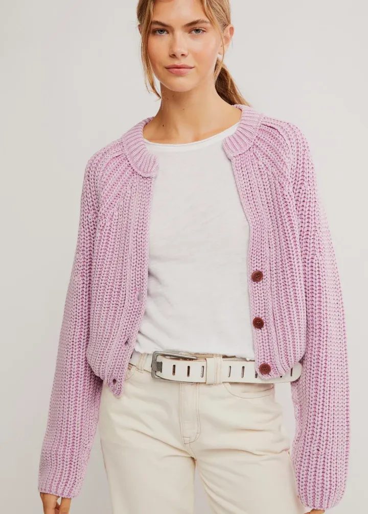 Woman wearing a pink knitted Free People Sweet Nothing cardigan over a white shirt with a plain