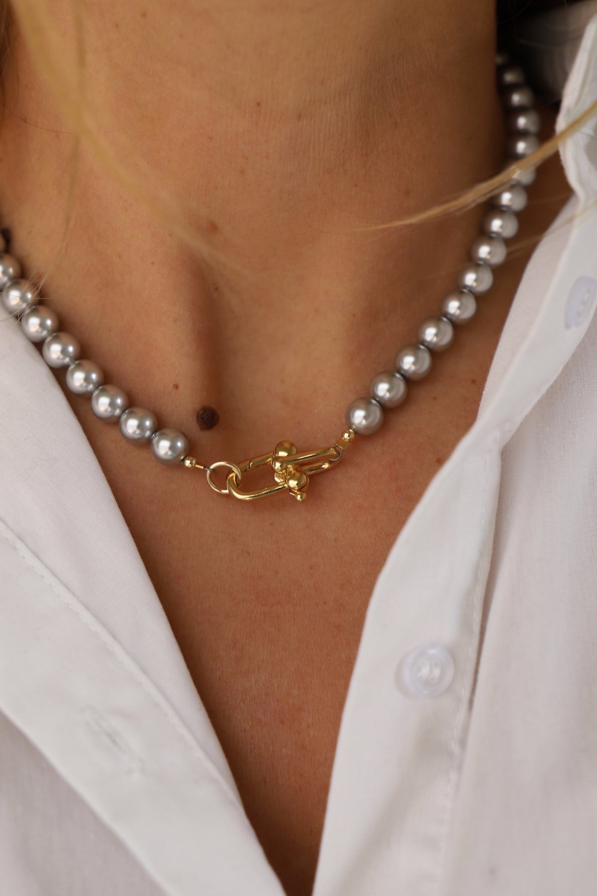 Pearl necklace with a gold clasp worn by a person wearing a white shirt.