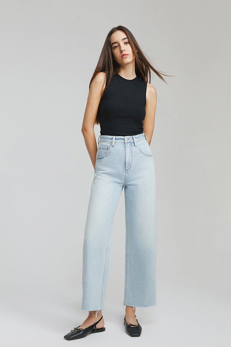 Woman wearing light blue jeans and a black top on a plain background