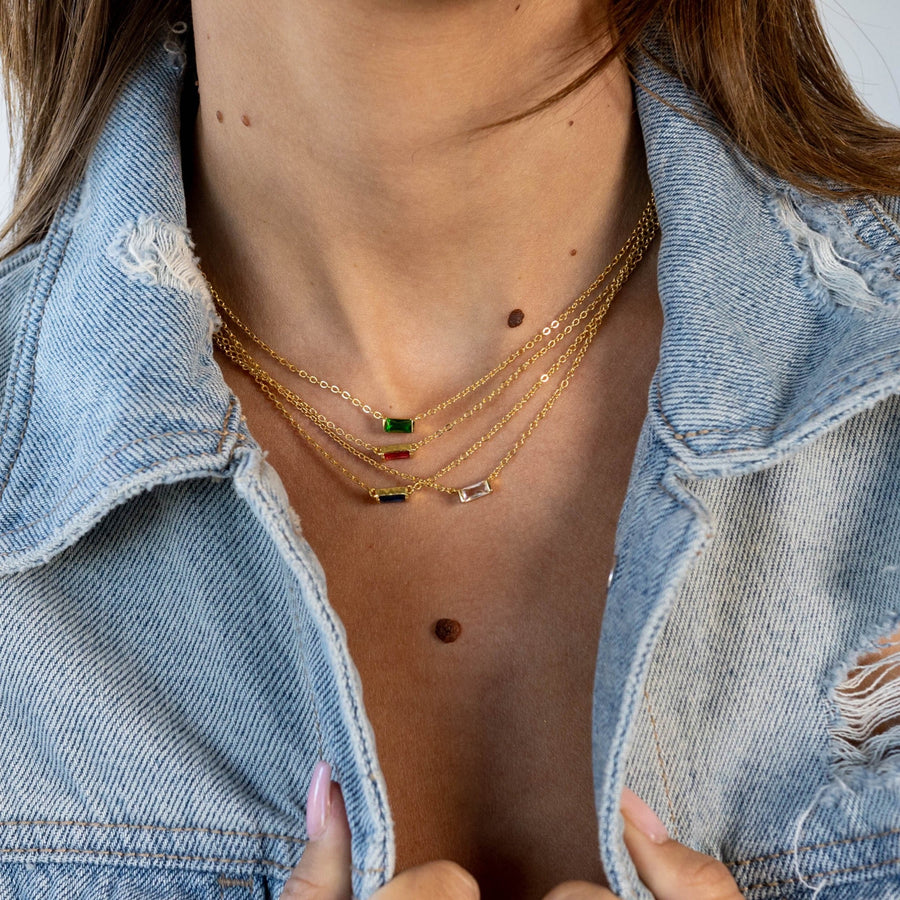 Close-up of a person wearing multiple gold necklaces with colored stones, partially covered by a denim jacket.