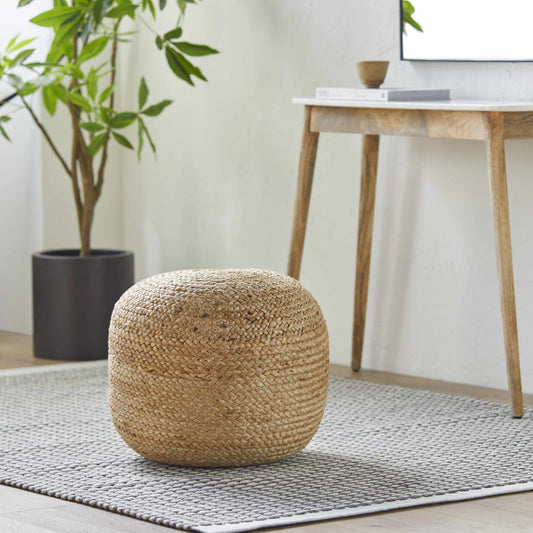 Woven ottoman on a rug with a plant and table in the background