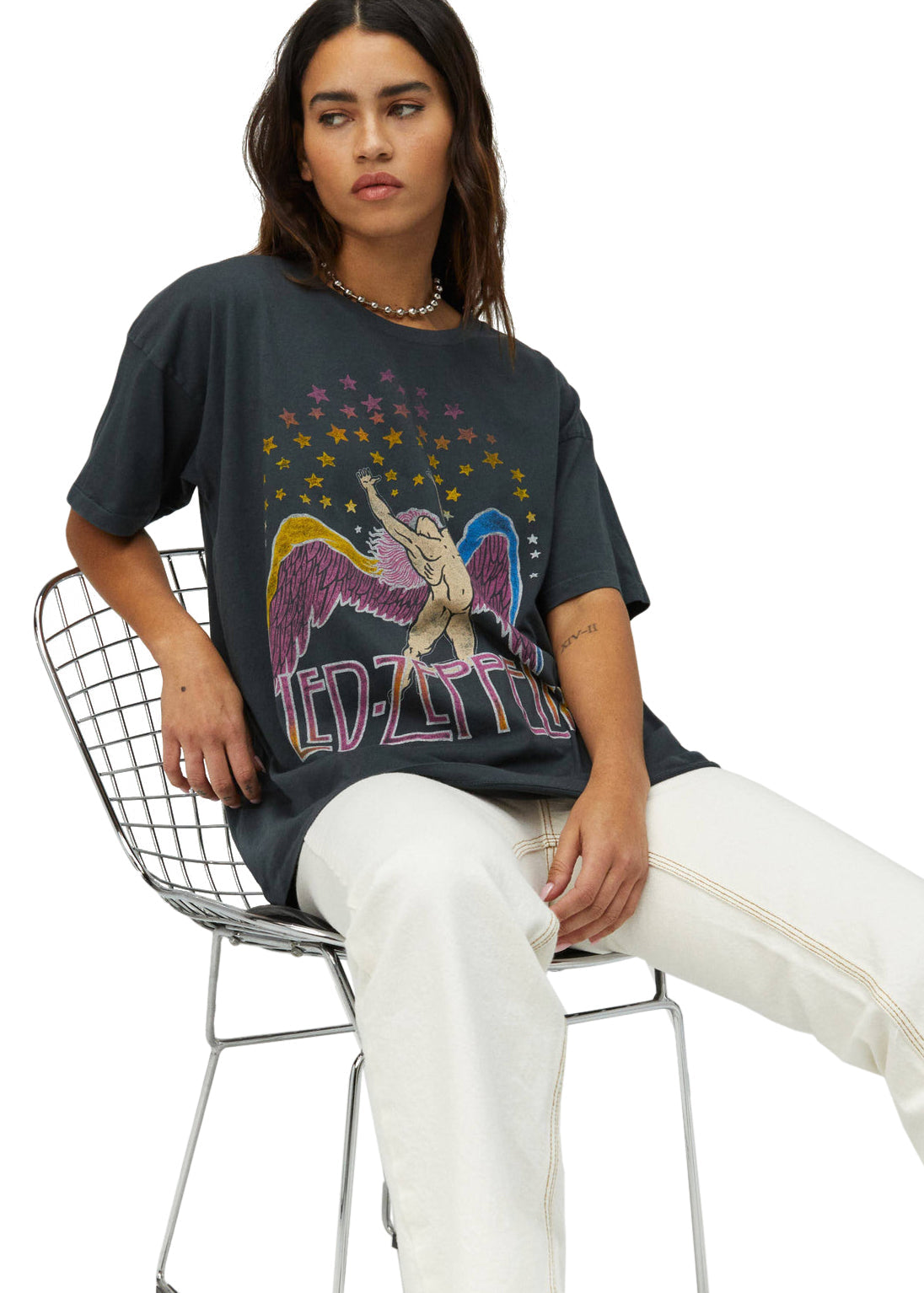 Person wearing a black t-shirt with a colorful graphic design, sitting on a metal chair.