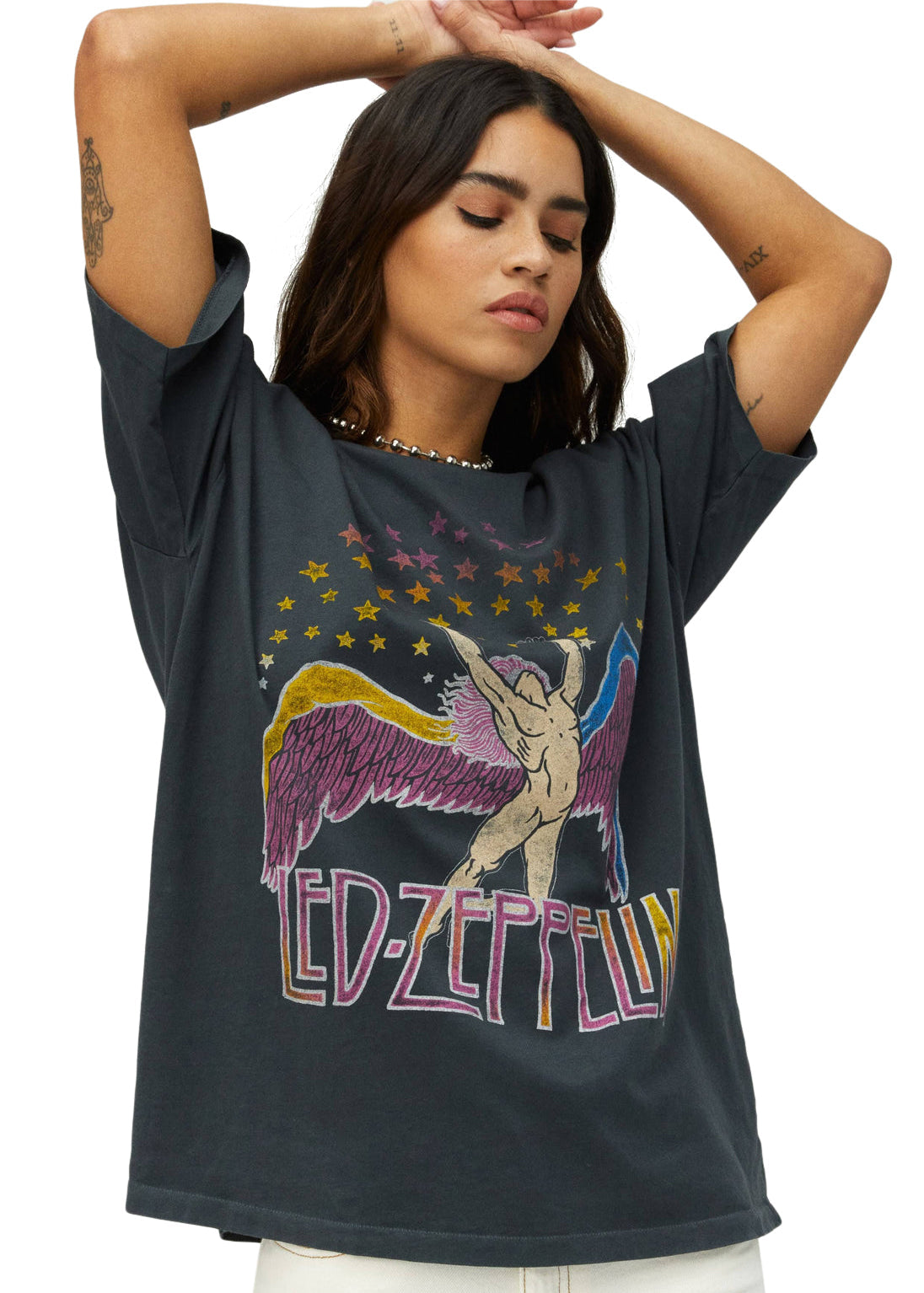 Woman wearing a black t-shirt with a colorful graphic design, possibly of a band name, on a plain background.