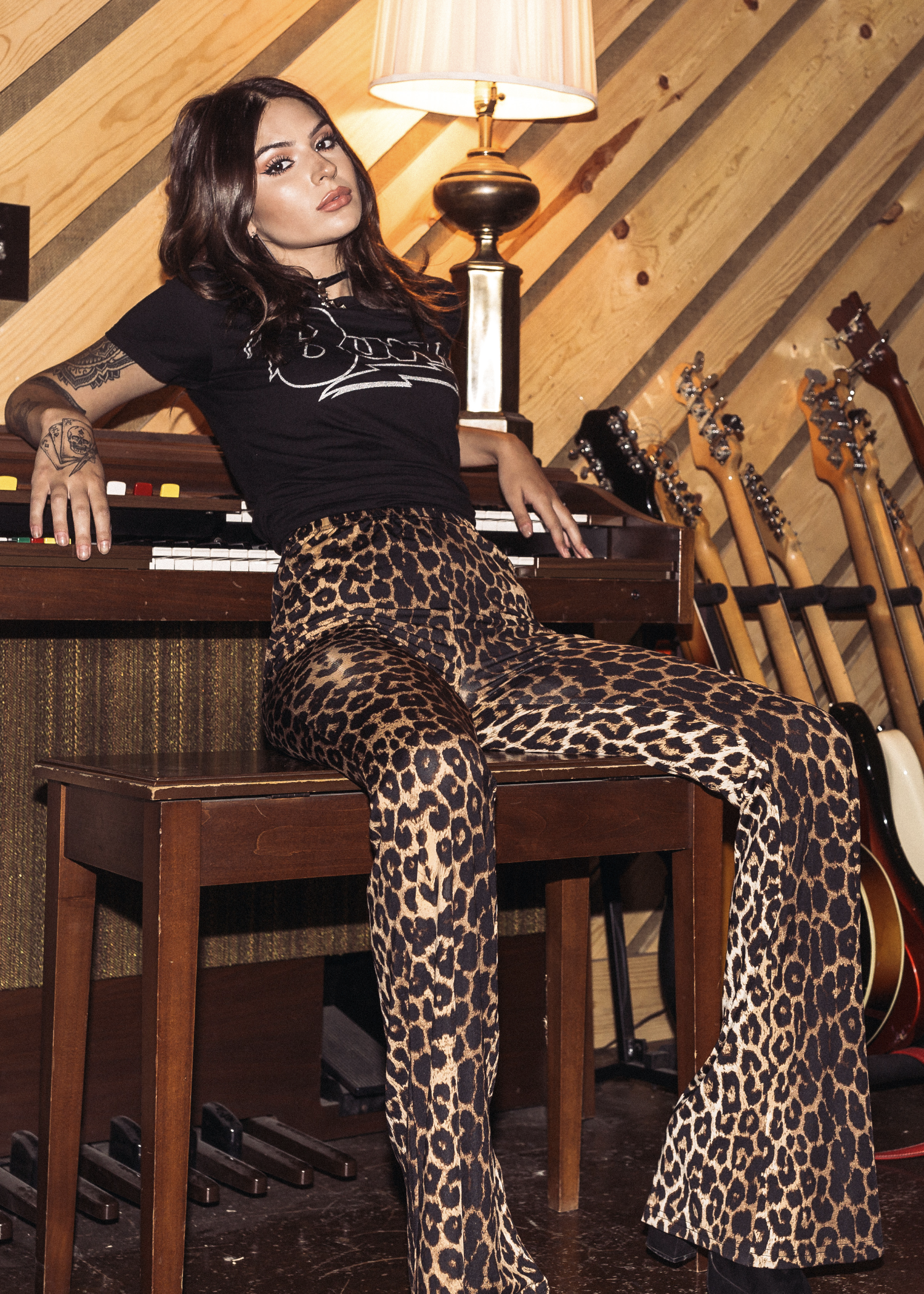 Woman in leopard print pants and black top sitting on a piano with guitars in the background